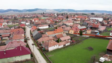 Aerial-View-Of-Transylvanian-Village-In-Sansimion,-Harghita-County,-Romania-With-Distant-View-Of-Ciuc-Mountains-In-Background