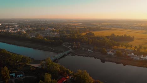 Eine-Luftaufnahme-Eines-Flusses-In-Polen-Bei-Sonnenaufgang-Mit-Einer-Grünen-Brücke-Und-Grüngelb-Im-Hintergrund