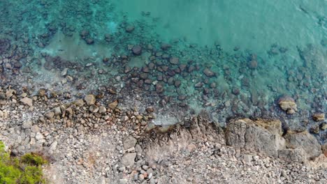 Beautiful-aerial-view-of-cliff-with-the-sea,-a-clear-blue-and-turquoise-sea-with-crystal-clear-and-calm-waters-lets-you-see-the-rocks-in-the-background-on-a-journey-from-left-to-right