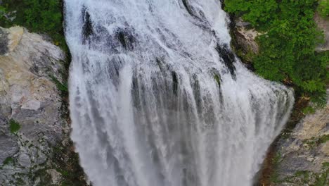 Atemberaubende-Luftaufnahme-Des-Majestätischen-Und-Mächtigen-Wasserfalls,-Der-Durch-Felsen-Inmitten-Steiler-Waldberge-Fließt