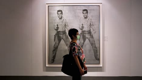 Ein-Besucher-Mit-Gesichtsmaske-Geht-An-Einem-Kunstwerk-Von-Andy-Warhol-Mit-Dem-Namen-„Doble-Elvis“-Vorbei,-Das-Den-Verstorbenen-Schauspieler-Und-Sänger-Elvis-Presley-Darstellt,-Bei-Der-Sotheby&#39;s-Show-Von-Brokers-Modern-Collectibles-In-Hongkong