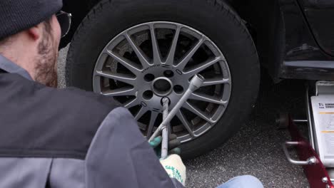Handyman-removing-seasonal-tires-with-a-cross-wrench,-over-the-shoulder
