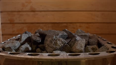 Closeup-shot-of-sauna-stones-with-water-being-pored-on-the-dry-stones,-wooden-panels-behind