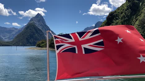New-Zealand's-Red-Ensign-Flag-On-Cruise-Ship-Waving-In-The-Wind-At-Milford-Sound-In-Fiordland,-New-Zealand