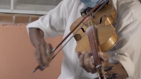 Closeup-shot-of-a-Hispanic-aged-musician-with-a-hat-and-a-mask-playing-violin-on-the-street