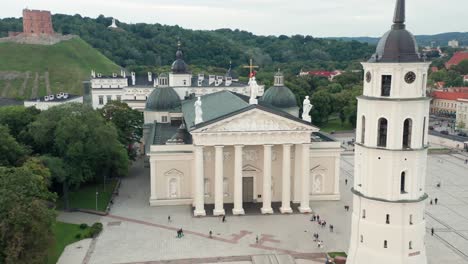 AERIAL:-Flying-Towards-Vilnius-Cathedral-and-Bell-Tower-While-People-Walks-on-Ground-During-Warm-Summer-Evening