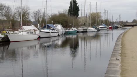 Small-sailboats-moored-on-narrow-empty-countryside-canal-marina