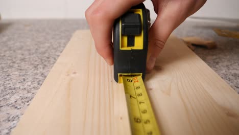 Caucasian-hand-of-handyman-rolls-out-a-yellow-measuring-tape,-dolly-in-shot