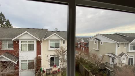 Looking-out-the-window-of-a-bedroom-of-a-three-story-townhouse-onto-the-neighbouring-homes-and-neighbourhood-with-mountains-and-grey-sky-in-the-background
