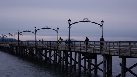 Static-view-of-people-walking-on-a-long-pier-leading-towards-a-break-water-in-ocean-during-the-evening-clouds-at-dusk