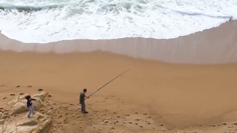 Top-view-of-man-with-his-daughter-fishing-on-the-beach