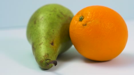 Fresh-big-green-pear,-juicy-orange-rotates-slowly-on-a-light-blue-background,-healthy-food-concept,-extreme-close-up-shot,-camera-rotate-left