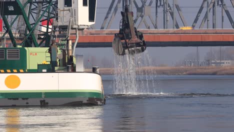 Rotating-crane-on-top-of-a-dredging-ship-in-front-of-a-bridge-clearing-the-waterway-of-river-IJssel-at-the-IJsselkade