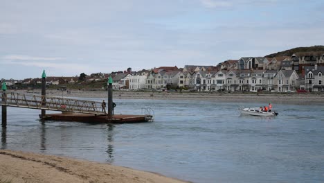 Small-boat-passing-two-men-waiting-on-metal-jetty-seafront-platform-overlooking-fishing-town
