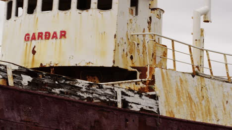 Abandoned-rustic-vessel-Gardar-on-Iceland-coastline,-quick-pan-left