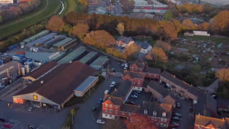 Golden-hour-aerial-view-over-supermarket,-allotments,-and-suburbs-in-Exeter,-UK