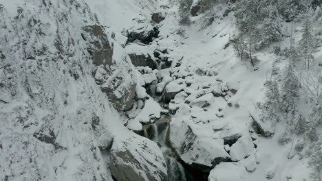 Aerial-of-series-of-small-waterfalls,-revealing-creek-in-snow-covered-valley