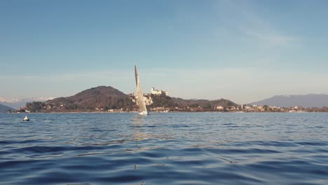 Low-angle-zoom-out-pov-of-sailboat-sailing-on-Maggiore-lake-with-and-Angera-castle-in-background