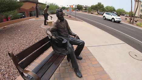 Una-Estatua-De-Bronce-Del-Presidente-Abraham-Lincoln-Se-Sienta-En-Un-Banco-Del-Parque-Viendo-Pasar-El-Tráfico,-Fountain-Hills,-Arizona