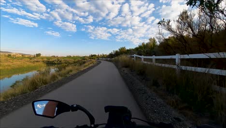 Cycling-along-a-paved-pathway-beside-a-river-with-the-sky-reflecting-off-the-water