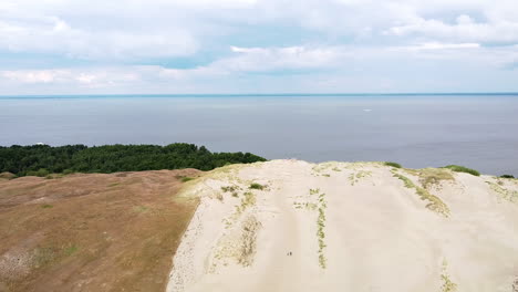 End-of-sandy-dune-with-view-to-Curonian-lagoon,-drone-descending-view
