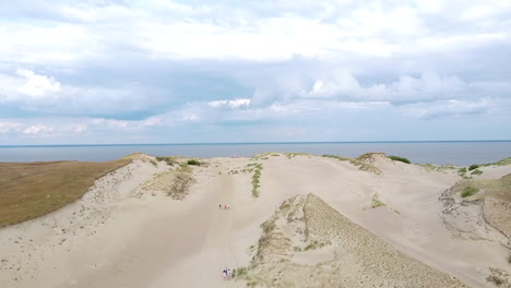 Sandy-dune-of-Neringa-while-people-walking-on-and-reveal-of-Curonian-lagoon,-ascending-drone-view