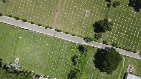 Aerial-overhead-view-of-a-cemetery-with-two-people-advancing-on-a-path-located-in-the-middle-of-white-headstones-arranged-in-rows