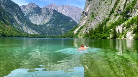 Man-diving-into-crystal-clear-water-of-idyllic-lake-surrounded-by-mountains,slow-motion-shot---Alps-Mountains-during-summertime-and-vibrant-colors