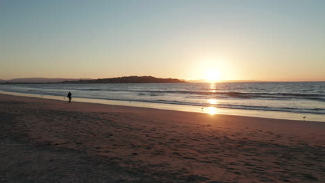 POV-Entlang-Des-Bei-Sonnenuntergang-Beleuchteten-Strandes-Von-Tongoy-In-Puerto-Velero-Mit-Langsam-Brechenden-Wellen-Und-Der-Silhouette-Einer-Vorbeigehenden-Person