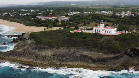 Vista-Aérea-Del-Faro-De-Arecibo-Y-La-Idílica-Playa-De-La-Poza-Del-Obispo-En-Arecibo,-Puerto-Rico---Toma-De-Drones