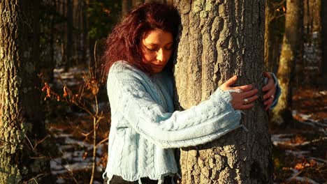 young-red-hair-caucasian-girl-hugging-a-tree-in-the-woods-at-sunset,-medium-shot