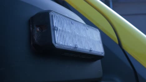 The-exterior-of-yellow-paramedic-ambulance-vehicle,-blue-flashing-warning-lights,-closeup-handheld-shot