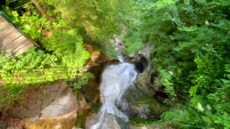 Zeitlupe-Von-Oben-Nach-Unten-Eines-Tosenden-Idyllischen-Wasserfalls-Zwischen-Grünen-Bergen,-4k