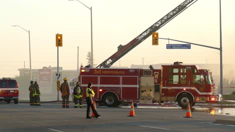 Road-blocked-on-the-surrounding-of-the-fire-area,-a-firefighter-climbing-down-from-an-aerial-ladder-while-the-fire-engine-parked-stationary-at-the-fire-scene,-Mississauga-fire-department