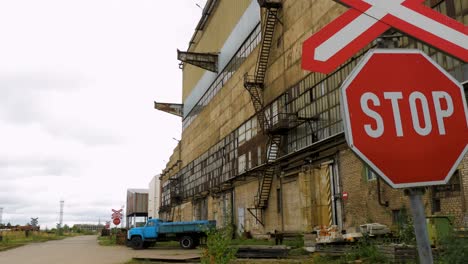 Exterior-view-of-abandoned-Soviet-heavy-metallurgy-melting-factory-Liepajas-Metalurgs-territory,-STOP-sign-at-railways,-blue-cargo-truck-in-background,-overcast-day,-wide-shot