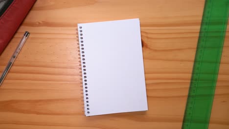 Hand-Places-Open-Notebook-With-Blank-Page-On-The-Table-With-Ruler-And-Ballpoint-Pen-On-The-Sides