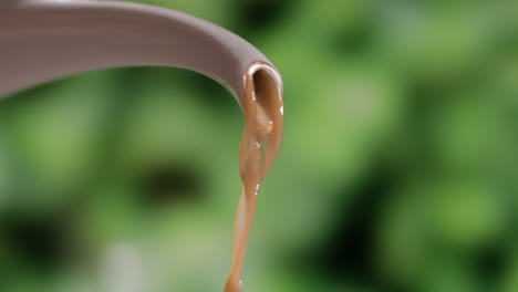 Close-Up-Of-Freshly-Brewed-Brown-Coffee-Pouring-From-Spout-Of-A-Porcelain-Kettle-Against-Blurry-Background