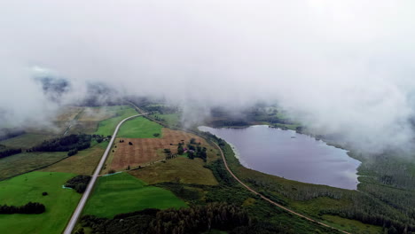 Aerial-view-of-a-landscape-with-a-lake,-forests-and-fields,-through-which-roads-lead-on-a-foggy-morning-with-a-dense-inversion-at-altitude