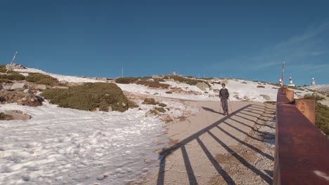 Front-view-of-Young-hiker-walking-down-a-Road-in-snowy-mountain-peak-in-Guadarrama-National-Park,-Madrid,-Spain