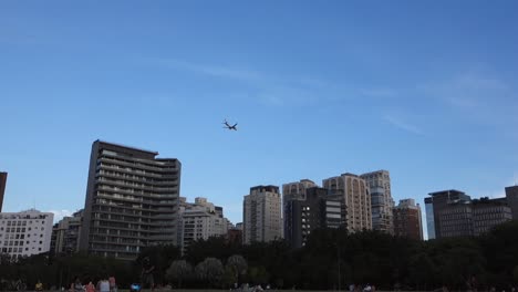 plane-flying-over-modern-buildings-in-the-city,-park-surrounded-by-skyscrapers