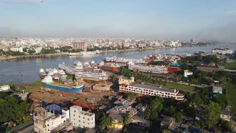 Aerial:-dockyard-at-Buriganga-river-bank-with-city-landscape-in-Dhaka,-Bangladesh---drone-establishing-shot