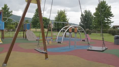 Empty-swings-swinging-in-children's-playground-on-gloomy-day