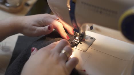 Close-up-of-cropped-female-hands-sewing-fabric-on-professional-manufacturing-machine