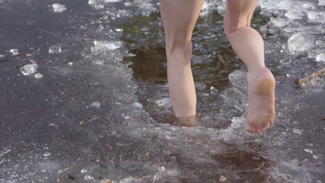 Beautiful-legs-of-a-young-woman-walking-into-icy-water,-jumps-out