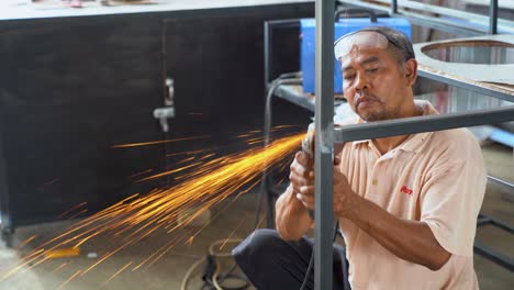 Worker-grinding-metal-welding-joints-of-metal-frame-in-Indonesia,-close-up-view