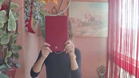 Charming-Young-Woman-Playing-Peek-a-boo-With-Red-Book,-Revealing-Face-With-Tongue-Out