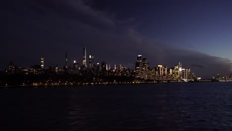 Horizonte-De-Manhattan-De-Nueva-York-Iluminado-Por-La-Noche-Con-Rascacielos-Y-Edificio-Moderno-Bajo-Una-Gran-Nube-Al-Atardecer