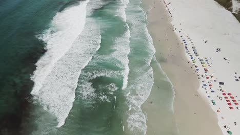 Waves-rolling-into-white-sand-beach-full-of-tourist-in-Rio-de-Janeiro,-Brazil