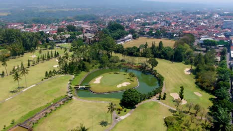 Tropical-golf-course-with-small-water-pond-and-island-with-holes,-aerial-orbit-view