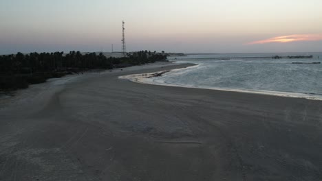 Long-shot-shot-with-drone-on-deserted-beach-at-sunset,-antenna-in-the-background-and-calm-sea,-wave